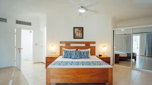 Une chambre à coucher avec un lit en bois, des lampes de chevet, un ventilateur de plafond, une porte et un grand miroir.