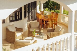 A covered outdoor seating area with wicker furniture, a table, and a potted plant.