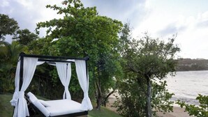 Uma cama privativa ao ar livre com dossel, cercada por vegetação exuberante e com vista para um corpo d'água.