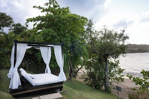 A private outdoor bed with a canopy, surrounded by lush greenery and overlooking a body of water.