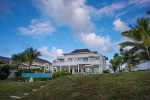 A two-story house with a balcony, surrounded by palm trees and a clear sky.