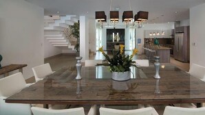 Uma zona de refeições moderna com uma mesa de vidro, cadeiras brancas e uma planta central.
