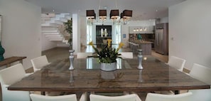 A modern dining area with a glass-top table, white chairs, and a central plant.