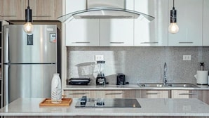 Une cuisine moderne équipée d’un réfrigérateur en acier inoxydable, d’un four encastré, d’une machine à café et d’un évier. On trouve trois tabourets en bois près de l’îlot central.
