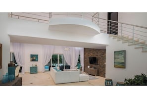 Uma sala de estar espaçosa com um sofá branco, parede de destaque em pedra e escada que dá acesso a um andar superior.