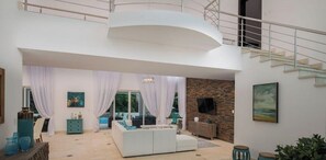A spacious living area with a white sofa, a stone accent wall, and a staircase leading to an upper level.