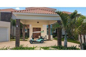 A modern house with a covered driveway, a golf cart, and palm trees.