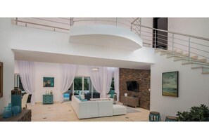 Uma sala de estar espaçosa com um sofá branco, parede de destaque em pedra e escada que dá acesso a um andar superior.