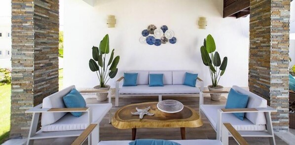 A cozy outdoor seating area with a sofa and chairs, a round wooden coffee table, and two potted plants.