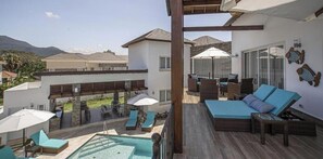 A rooftop terrace with a pool, lounge chairs, and a seating area with umbrellas.