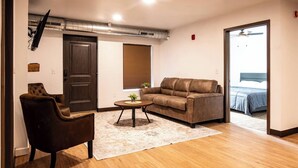 A living room with a brown leather sofa, a brown armchair, a small round coffee table with a plant, and a wooden floor. - Brillion 2‑Bedroom Suite w/ Full Kitchen Near Ariens - Unit # 3 (Brillion)