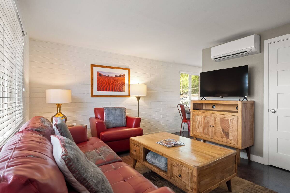 Una sala de estar moderna con un sofá rojo, una mesa de centro de madera, un televisor y un mueble.
