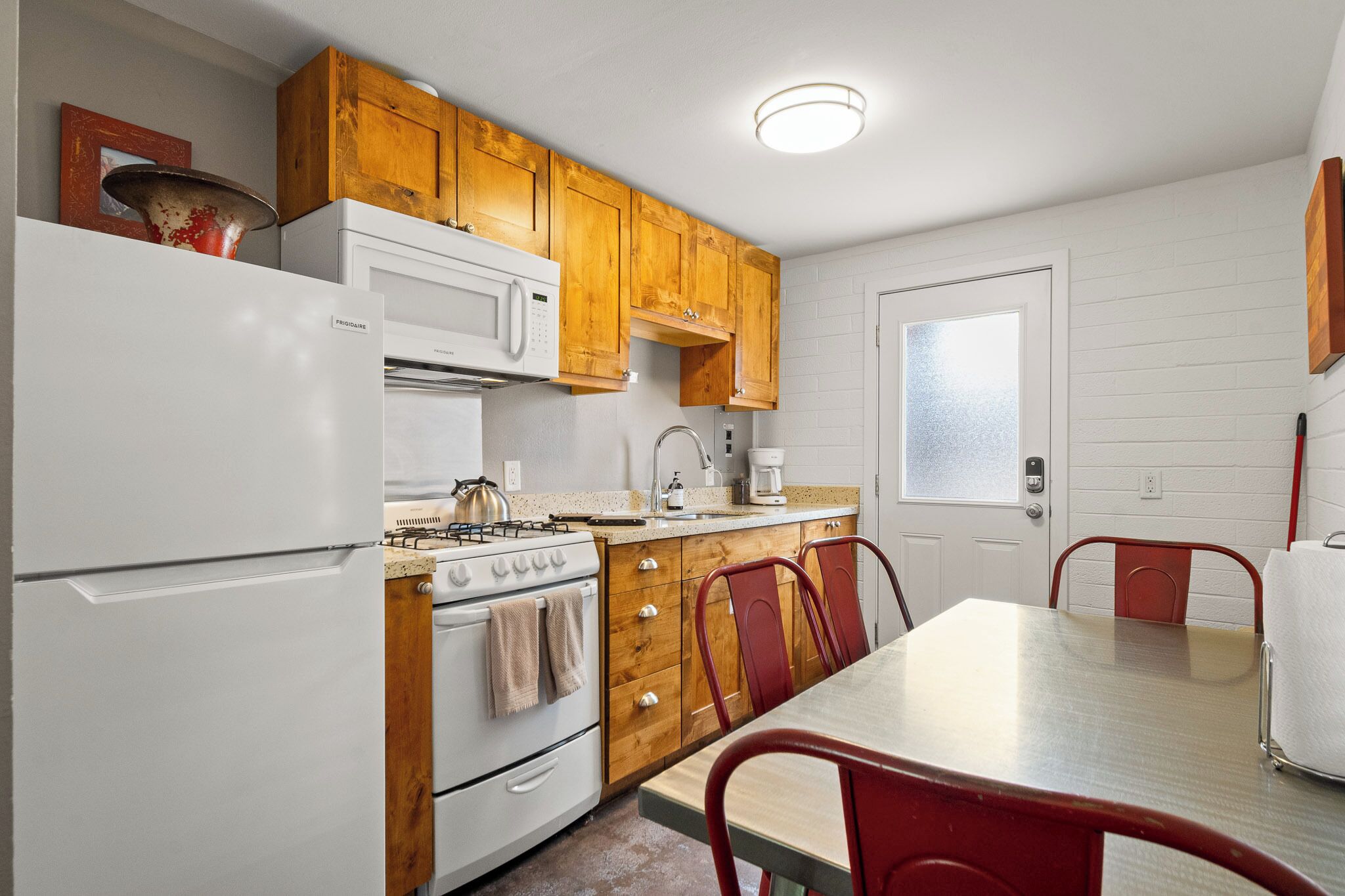 Une cuisine de taille réduite avec des meubles en bois, un réfrigérateur blanc, une cuisinière et une table à manger avec des chaises rouges.