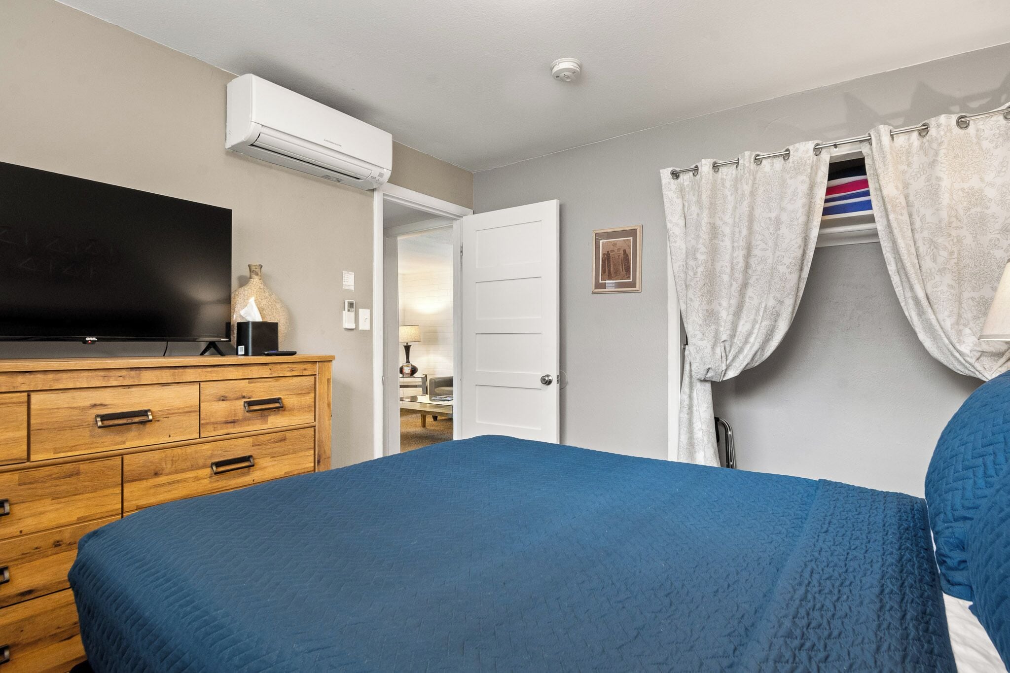 A bedroom with a bed, dresser, TV, and an air conditioning unit.