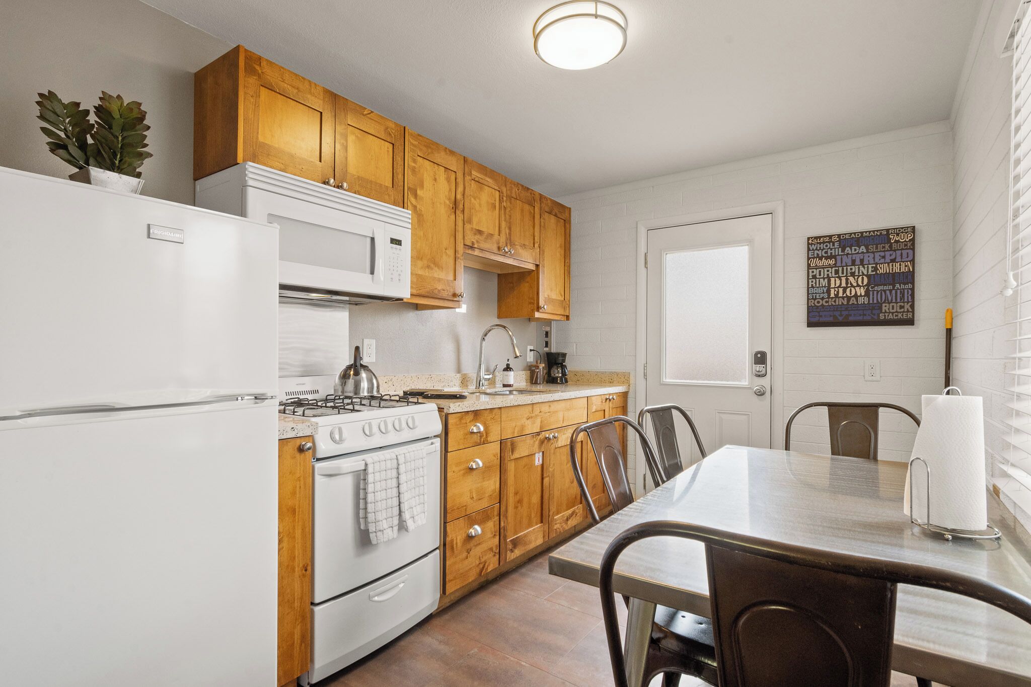 A kitchen with wooden cabinets, a white refrigerator, a stove, and a dining table with chairs.