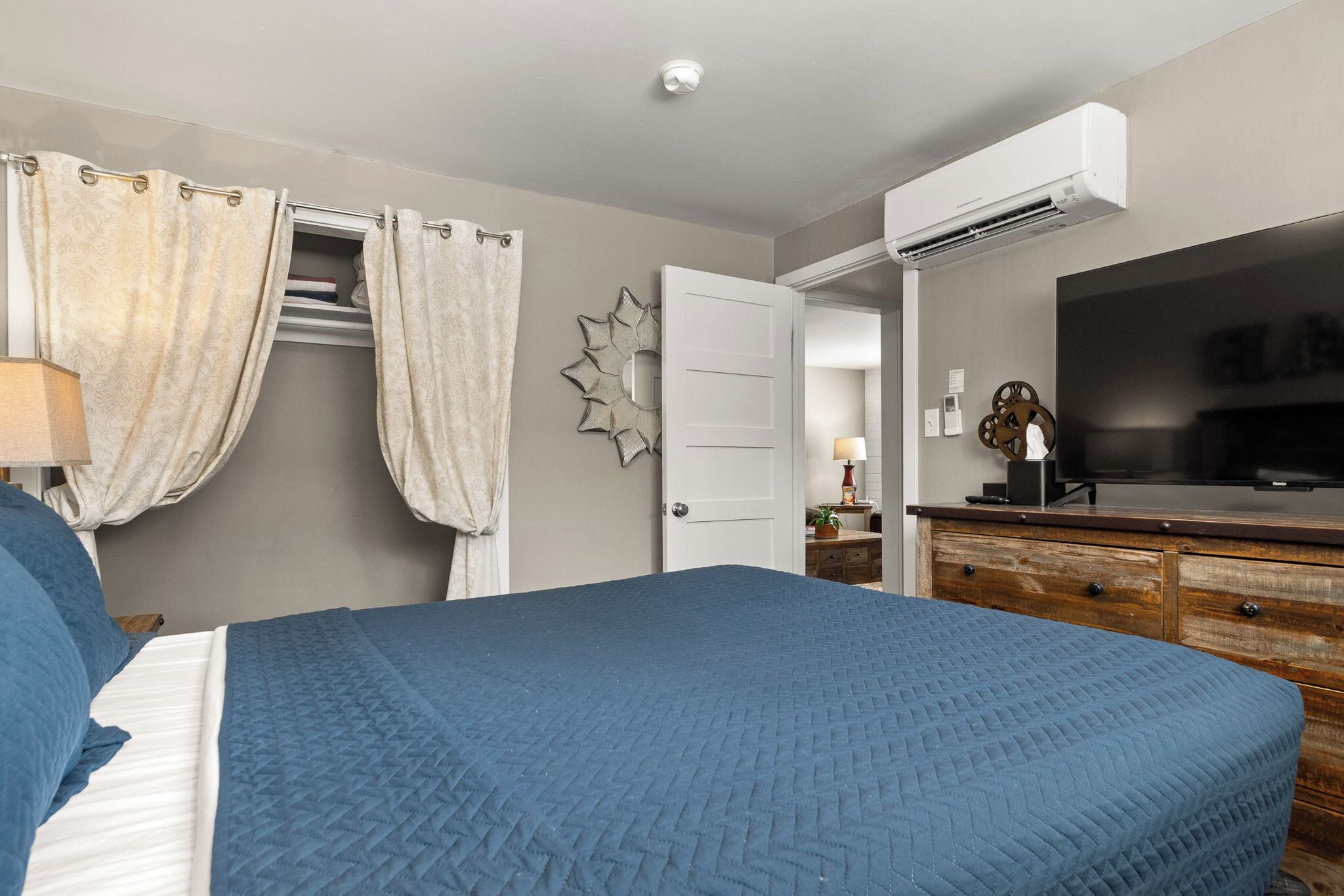 A bedroom with a large bed, a wardrobe, a television, and an air conditioning unit.