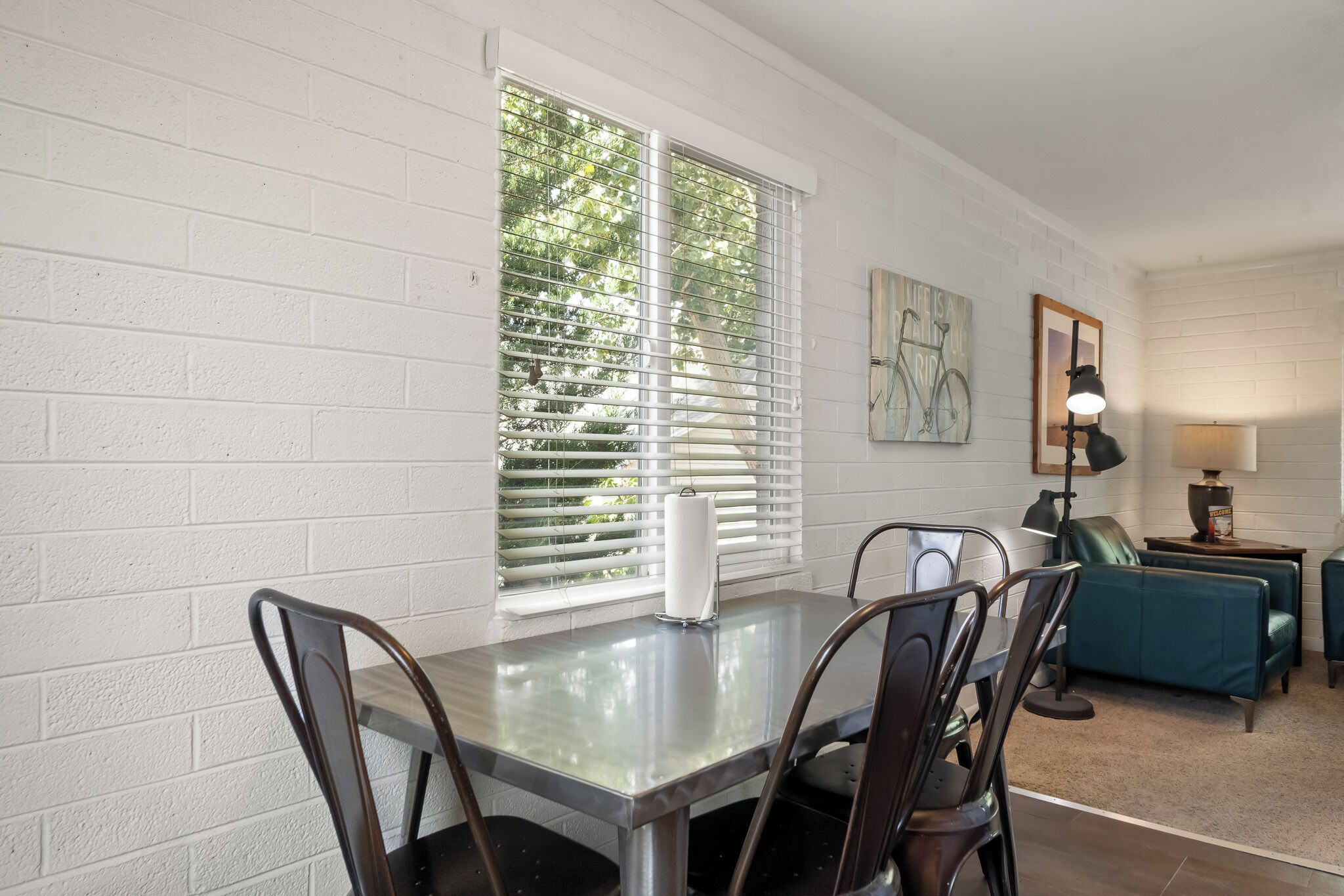 Un comedor con una mesa y sillas, una ventana con persianas, un sofá y una lámpara.