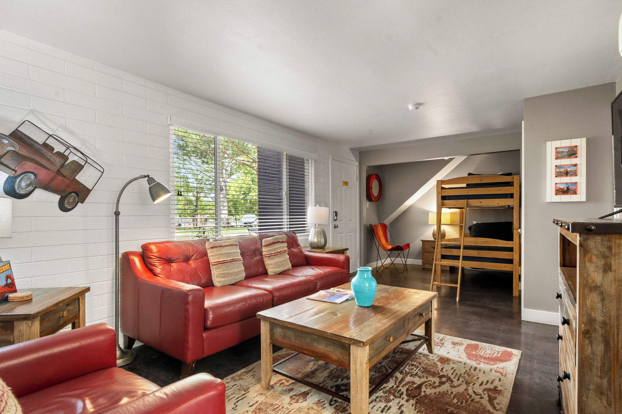 A cozy living room with a red leather sofa, a wooden coffee table, and a bunk bed in the background.