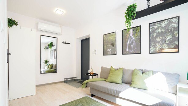 Una sala de estar moderna con un sofá gris, cojines verdes, una alfombra verde y cuadros en la pared.