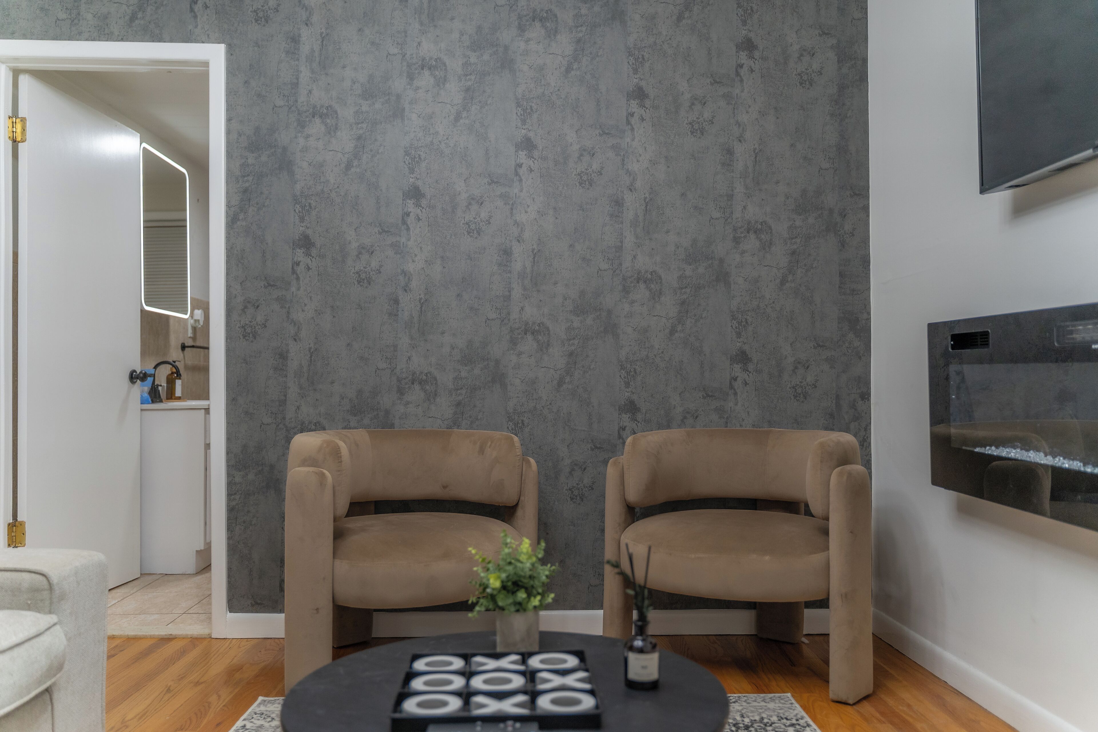 Un salón moderno con dos sillones color beige, una mesa redonda y una pared gris con textura.
