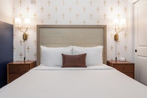 Ein ordentlich bezogenes Bett mit weißen und braunen Kissen, zwei Nachttische mit Lampen, und eine Wand mit einem floralen Muster.