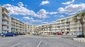 Een hotel met meerdere verdiepingen, balkons, een parkeerplaats en palmbomen.