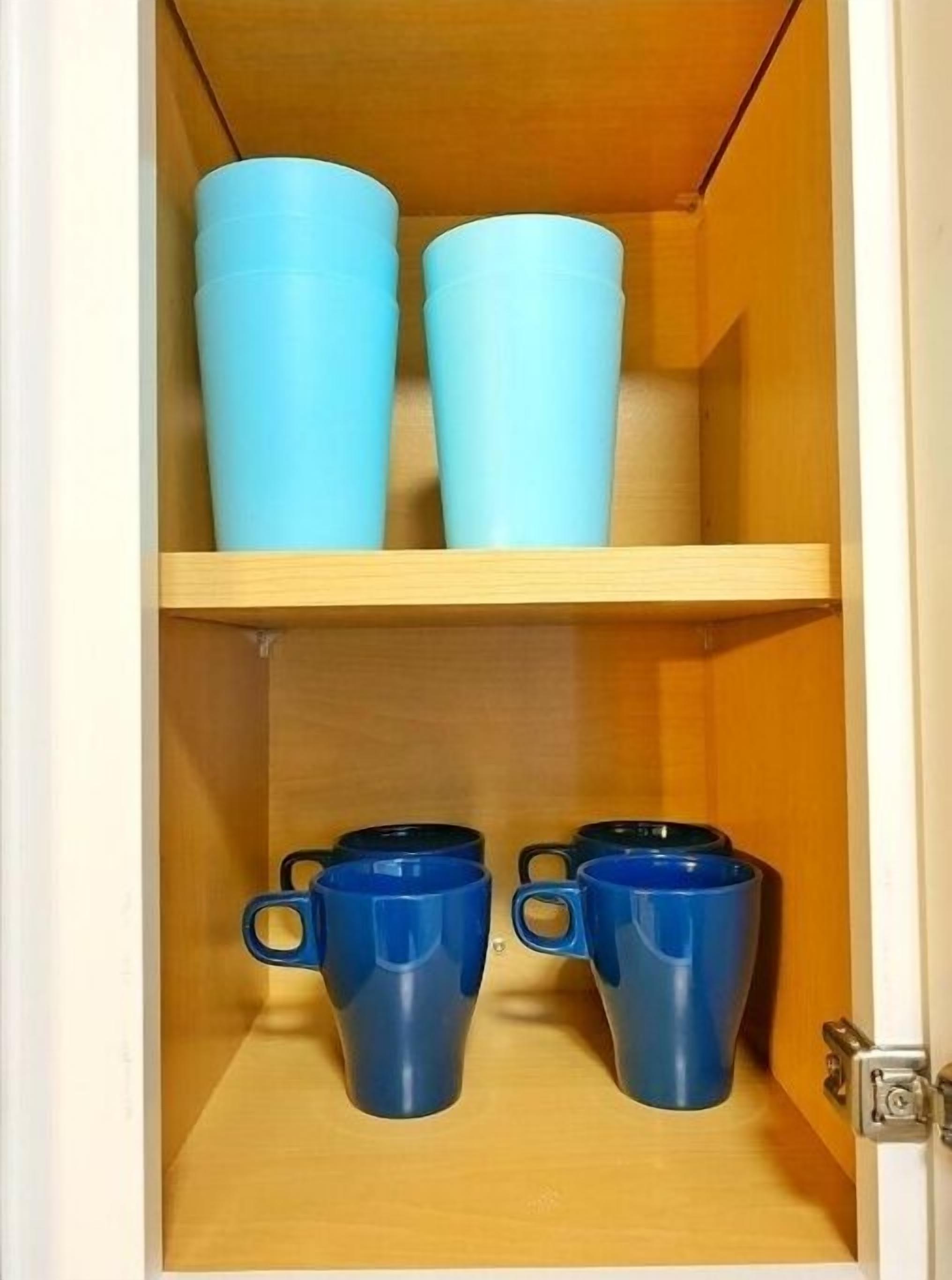 Un meuble en bois doté de deux étagères ; l’étagère supérieure contient deux récipients bleu clair, et l’étagère inférieure contient deux tasses bleu foncé.