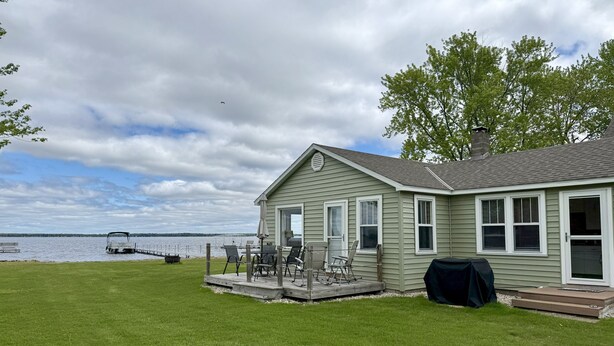 A house with a deck overlooking a lake, a boat docked, and a grill on the deck.