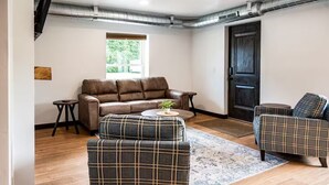 A living room with a brown leather sofa, two plaid armchairs, a small round coffee table, and a patterned rug. - Brillion 2‑Bedroom Suite w/ Full Kitchen Near Ariens – Unit #4 (Brillion)