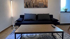 A living room with a black sofa, a wooden coffee table, and a cityscape painting on the wall. - ❤ VipStay Stylish 57m² ground-floor app., kitchen, terrace, Wi-Fi. Near S-Bahn ❤ (Eschelbronn)