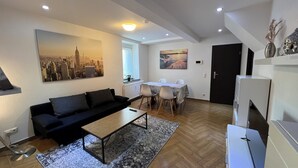 A modern living room with a black sofa, a wooden coffee table, and a patterned rug. There is a dining area with a white table and chairs, and a black door in the background. - ❤ VipStay Stylish 57m² ground-floor app., kitchen, terrace, Wi-Fi. Near S-Bahn ❤ (Eschelbronn)