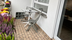 En terrasse med flisegulv, et bord og stole, et vindue og plantekrukker.