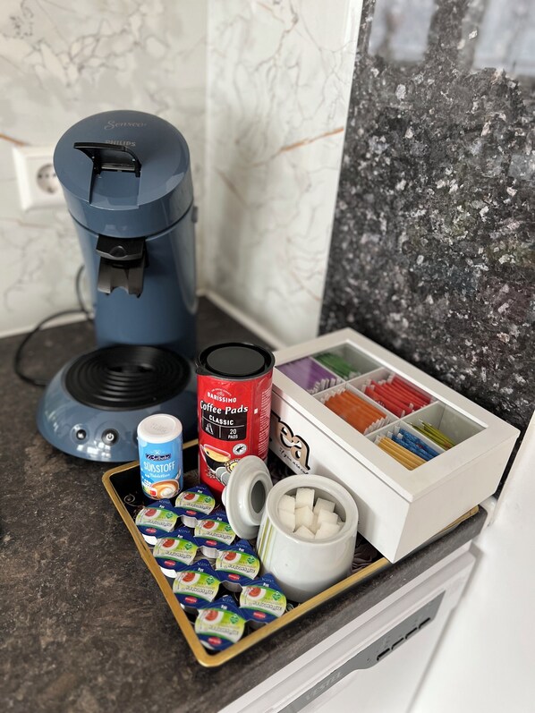 Un plan de travail de cuisine avec une machine à café, une boîte de dosettes de café, un récipient à sucre et un organiseur de tiroir.