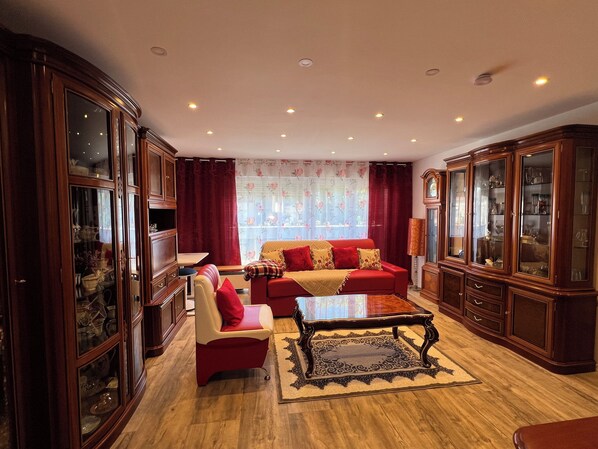 Ein geräumiges Wohnzimmer mit einem roten Sofa, einem passenden Sessel und einem Couchtisch. An beiden Seiten befinden sich Holzschränke mit Glastüren.