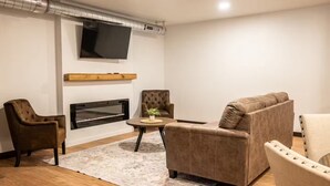 A modern living room with a fireplace, leather sofas, a television, and a wooden floor. - Brillion 2‑Bedroom Suite w/ Full Kitchen Near Ariens – Unit #5 (Brillion)