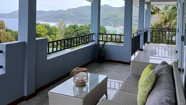 Un balcon abrité avec un canapé, une table basse en verre et une plante en pot.