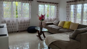 Un salon avec un canapé, une table basse en verre, un vase de fleurs et un ventilateur de plafond.