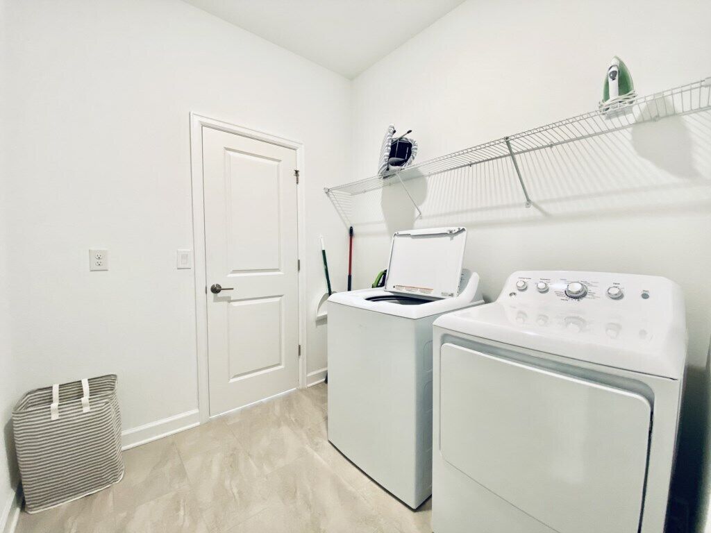 A laundry room with two white washers and dryers, a metal drying rack, and a door.