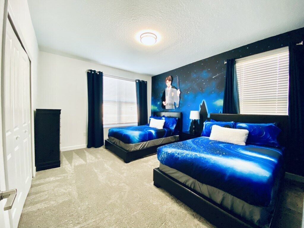 A bedroom with two beds, a nightstand, a wall mural, and a window with blinds.