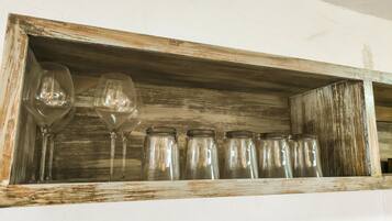 A rustic wooden shelf with two wine glasses and six glass jars.
