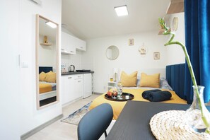 A modern hotel room with a bed, a dining area, and a kitchen.