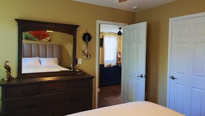 Une chambre à coucher comprenant un lit, une commode, un ventilateur de plafond et une porte donnant sur une autre pièce.