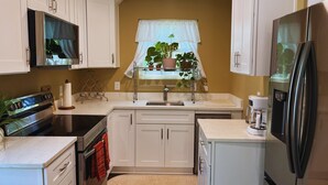 Une cuisine de taille réduite, avec des meubles blancs, un réfrigérateur en acier inoxydable, une cuisinière et un évier.