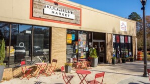 Un bâtiment sur lequel on peut lire l’inscription « Oakhurst Market », avec une terrasse extérieure dotée de chaises et de tables rouges.