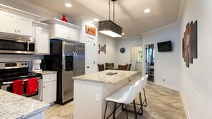 A modern kitchen with white cabinetry, stainless steel appliances, a granite countertop, and a bar area with white bar stools. - The Adele @ Oxford Farms- Tucked off South Lamar! Two Miles from The Square! (Oxford)
