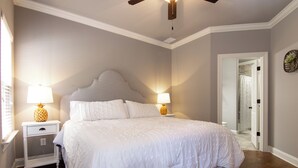 A bedroom with a large bed, two bedside tables with lamps, a ceiling fan, and a door leading to another room. - The Adele @ Oxford Farms- Tucked off South Lamar! Two Miles from The Square! (Oxford)