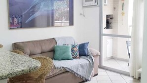 A living room with a sofa, a dining table, and a ceiling fan. There is a large window and an air conditioning unit on the wall. - Apartment in Ingleses Norte Floriañópolis (Florianópolis)