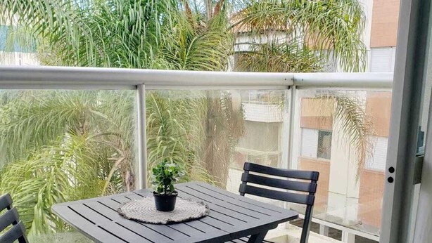 A balcony with a table and chairs, surrounded by lush greenery. - Apartment in Ingleses Norte Floriañópolis (Florianópolis)