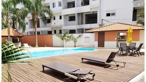 A wooden deck with two sun loungers, a pool, and a small outdoor dining area with chairs and a yellow umbrella. - Apartment in Ingleses Norte Floriañópolis (Florianópolis)