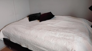 Una cama con edredón blanco estampado, dos almohadas y una mesita de noche con lámpara.